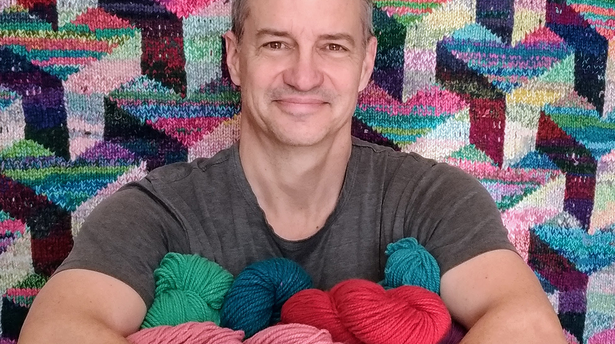 A man standing is smiling, holding several balls of yarn in his arms.
